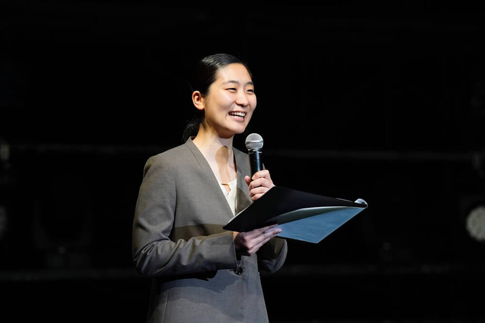 マイクを持って司会を行うスーツ姿のパフォーミングアーツ学科の女子学生
